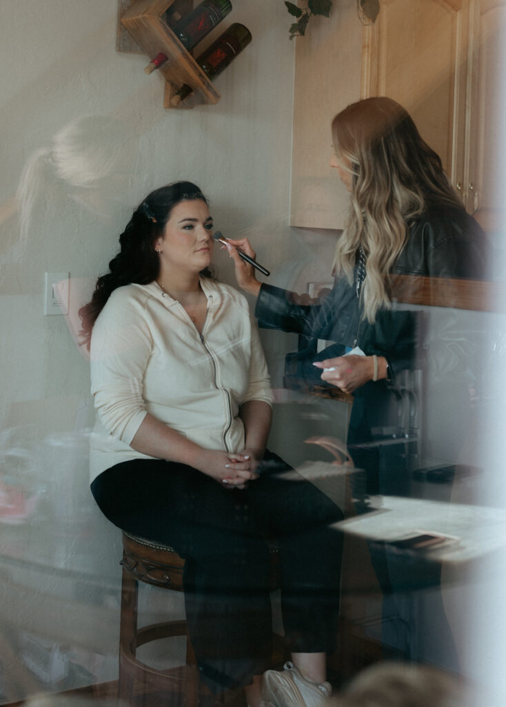 Woman sitting in a chair while having hair and makeup done.