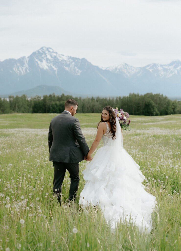 Couple walking in a field together for portraits during their Alaska wedding