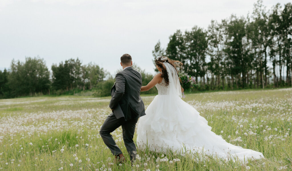 Couple wearing wedding attire while frolicking in a field of dandelions.