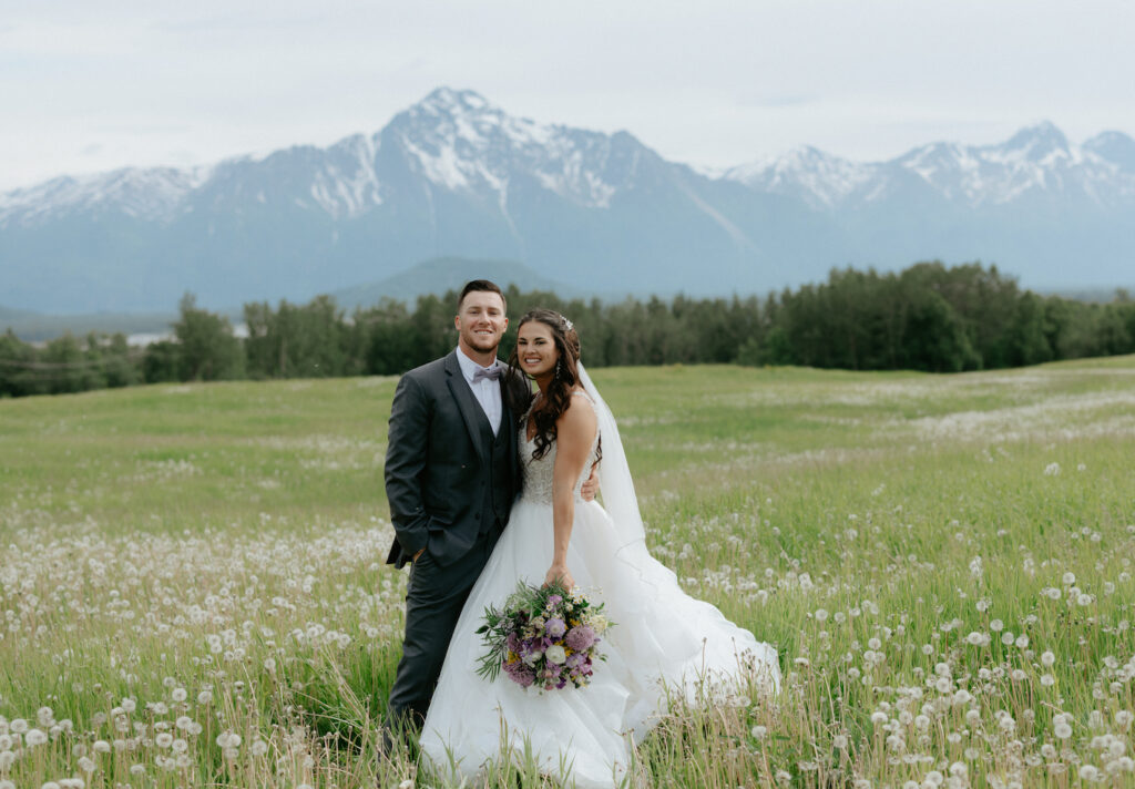 Couple embracing one another while standing in a field of dandelions for portraits during their wedding