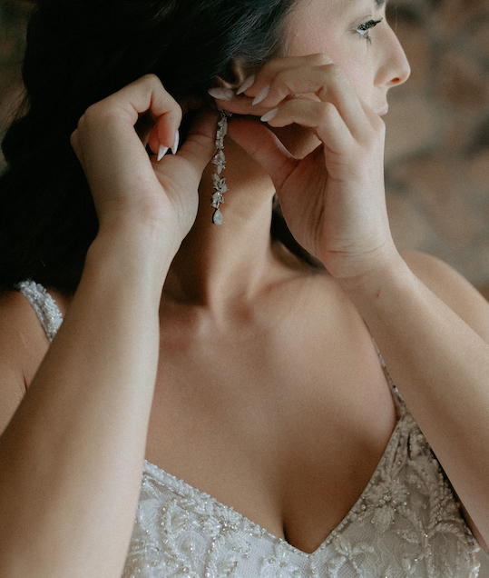 Woman putting on earrings while standing in front of a window during her Alaska wedding.