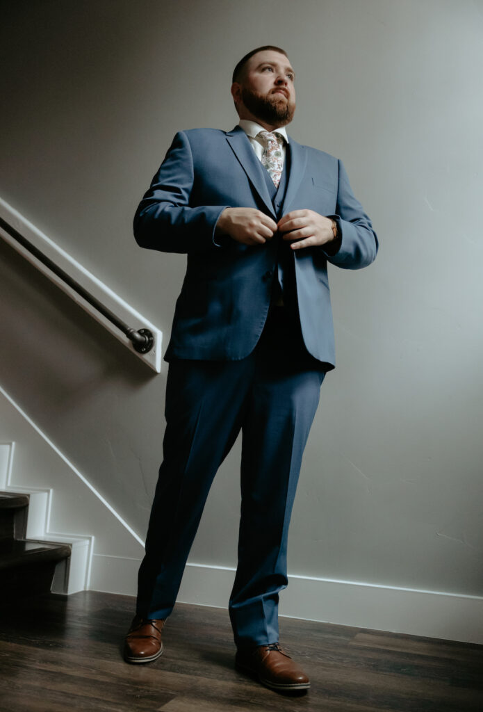 Man adjusting his jacket while facing a window inside a home. 