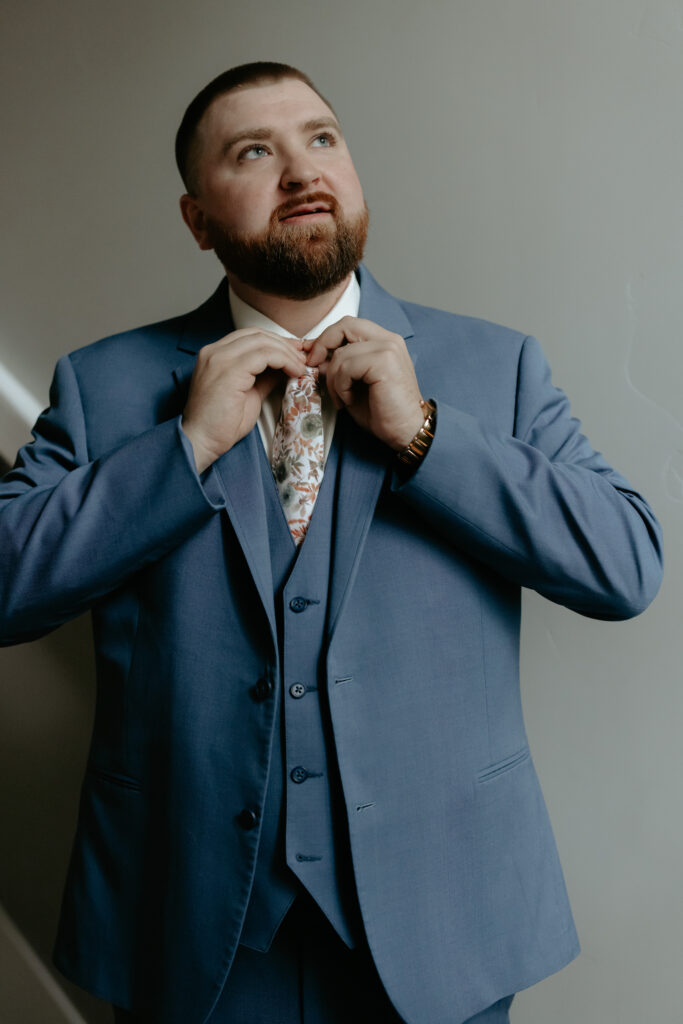 Man adjusting his tie while looking out a window.