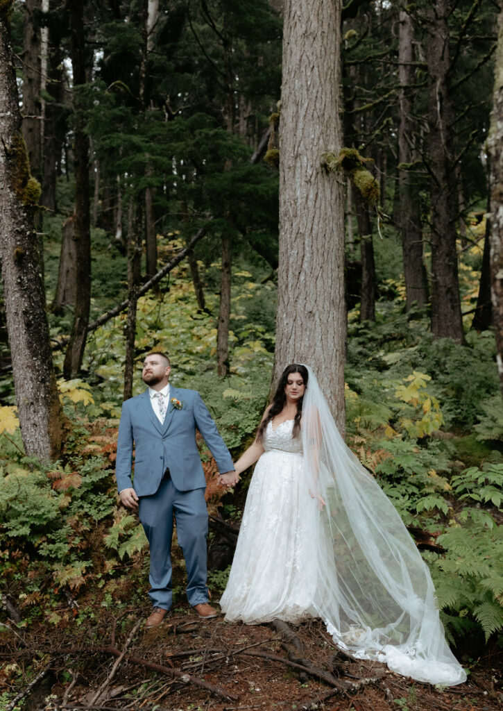 Man and woman looking in different directions while standing in a lush green forest 