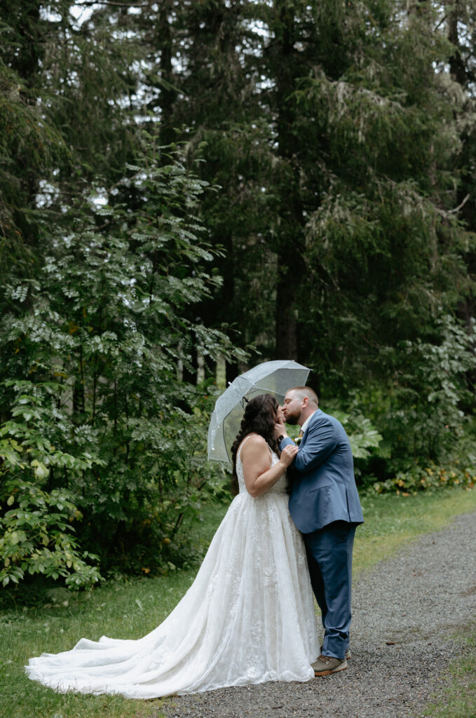 Man and woman standing under one umbrella and sharing a kiss with one another