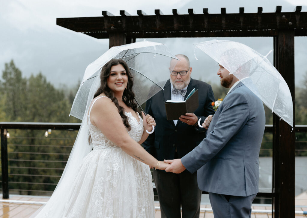 Man and woman holding hands and umbrellas while standing with their officiant at the altar. 