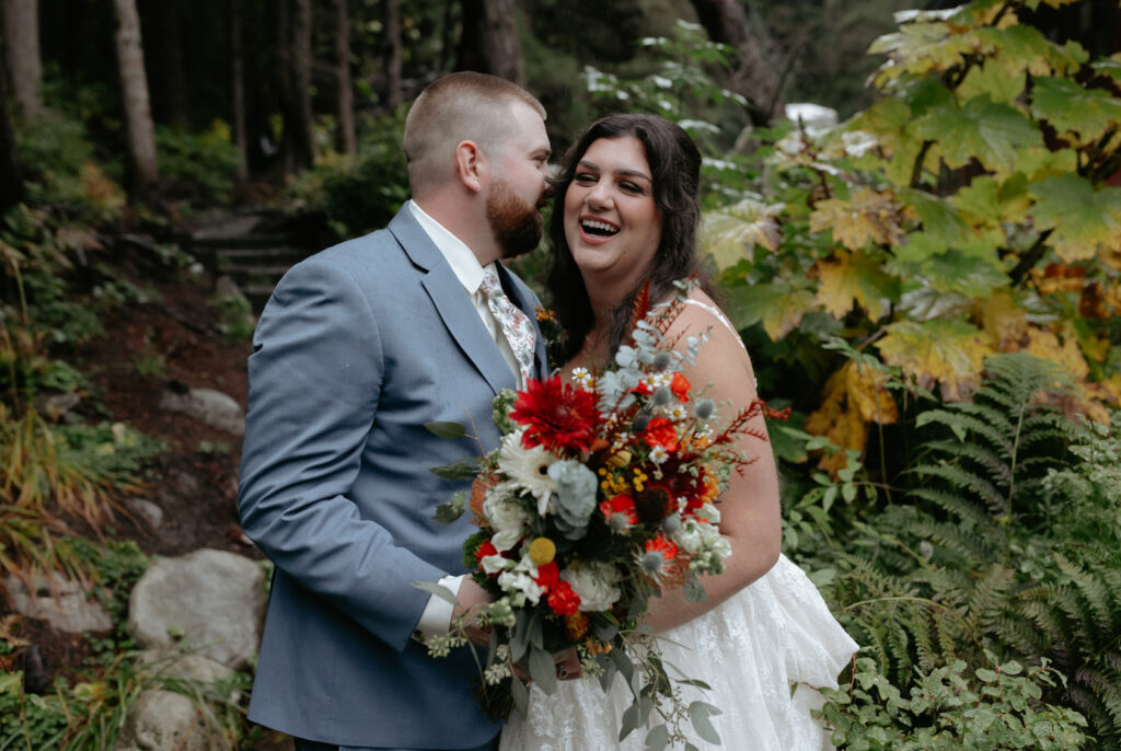 Man whispering in a woman's ear while she holds a colorful bouquet of flowers.