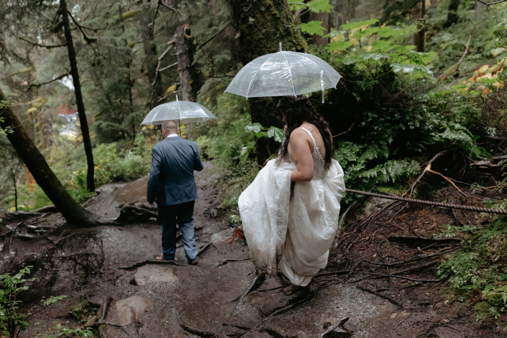 Man and woman carrying umbrellas while walking through a lush forrest. 