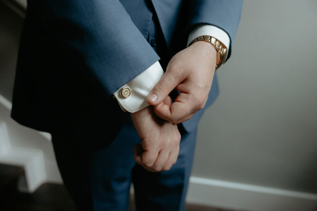 A pair of hands adjusting the sleeves and showing off a cufflink on a mens suit. 