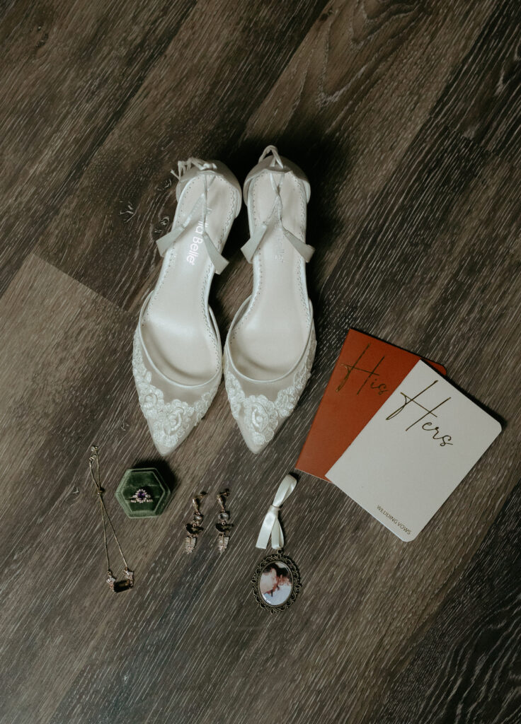 A woman's pair of shoes on a dark floor surrounded by a ring box containing a ring, a necklace and a pair of earrings.