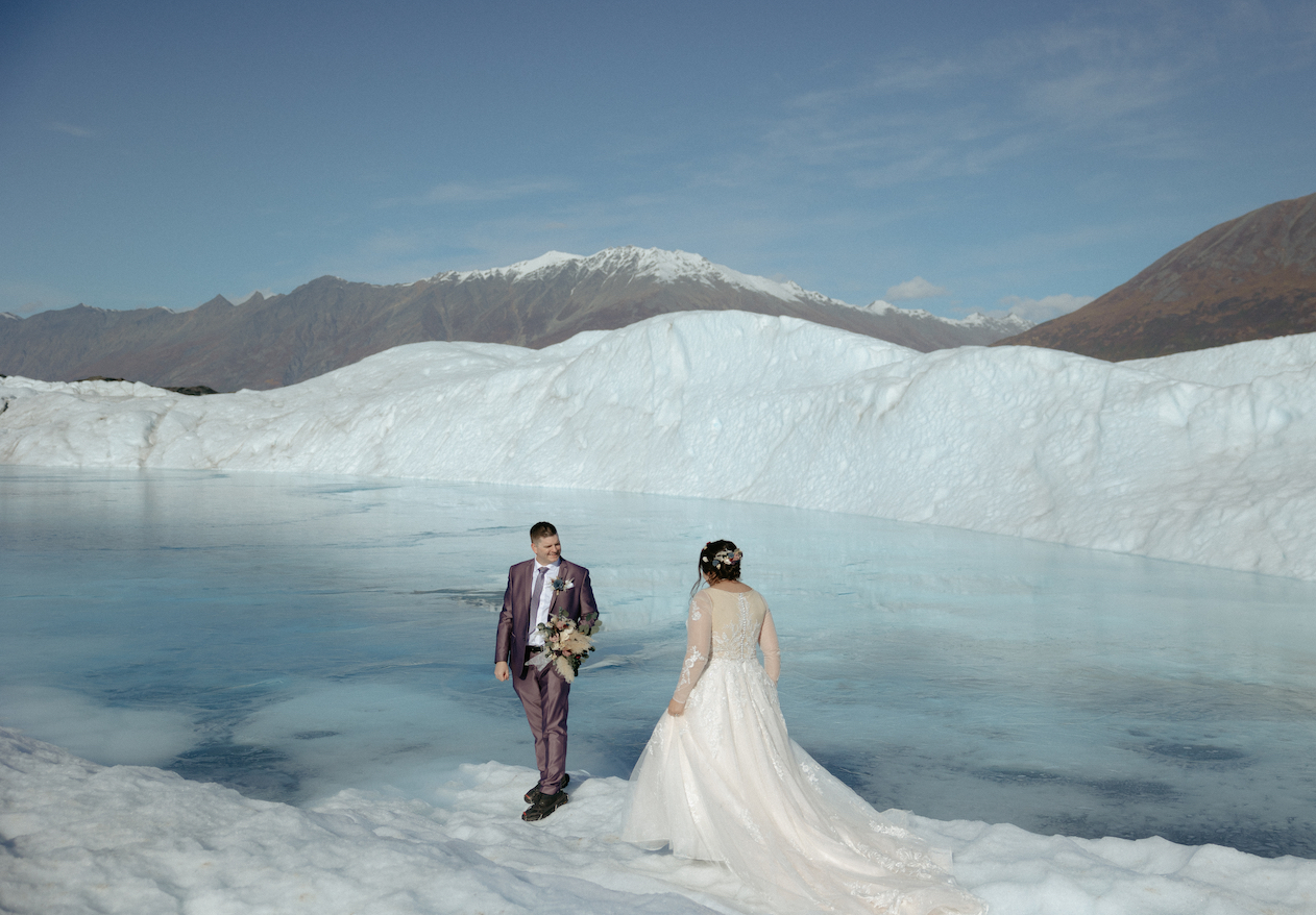 Woman wearing a white dress walking on a glacier in Palmer, Alaska. The couple pictured chose the Knik Glacier as the perfect venue for their Alaska wedding. 