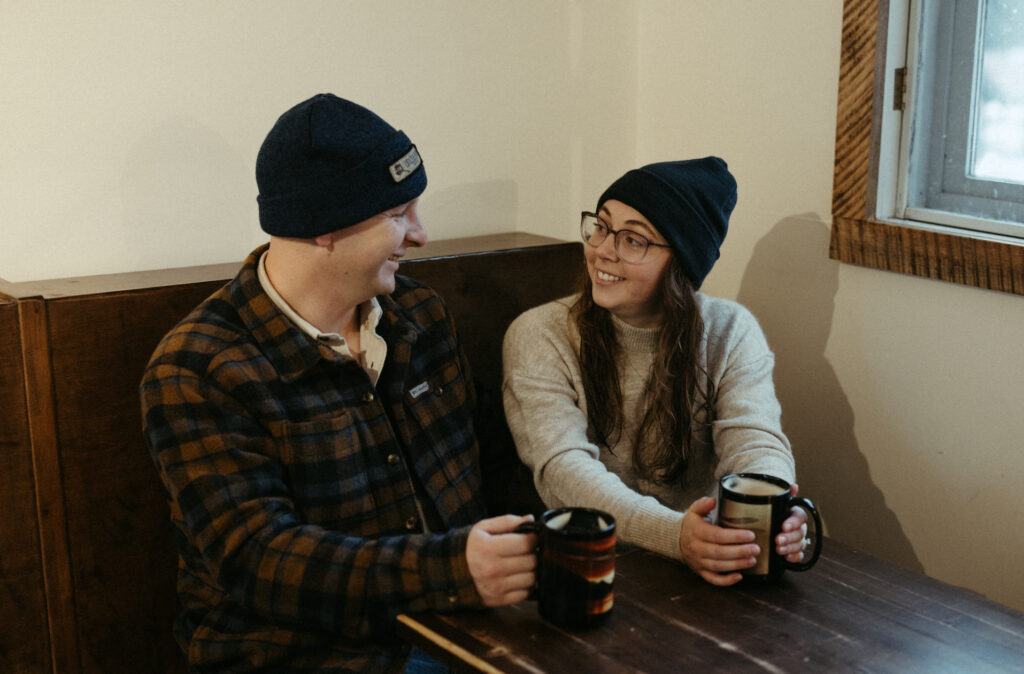 A couple interacting with one another while sitting on a bench inside a coffee shop. 