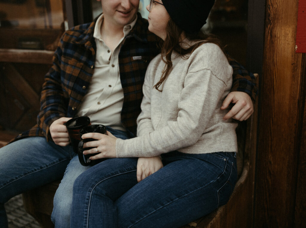 A couple sitting together on an outdoor bench at a coffee shop.