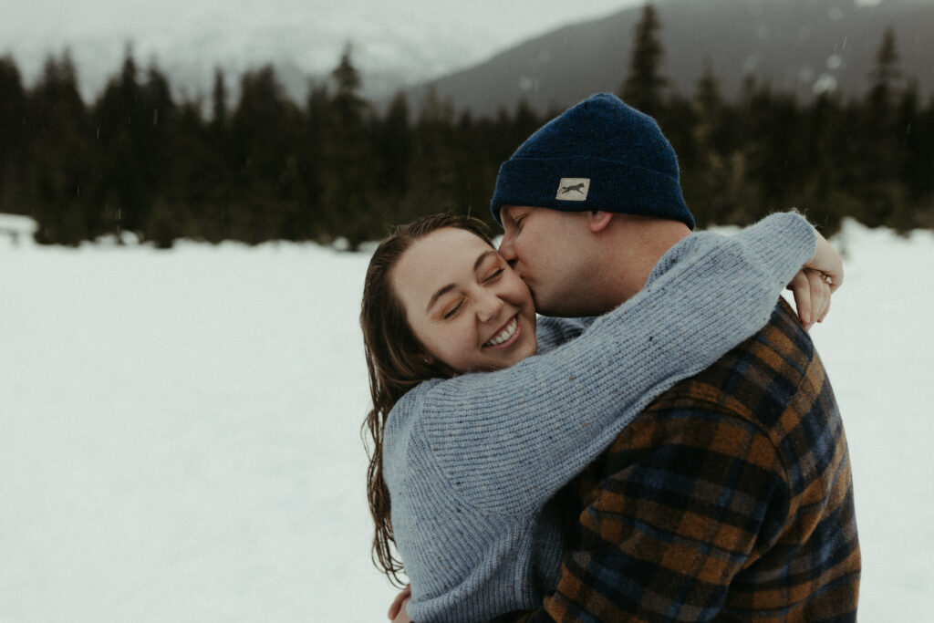 Man kissing woman on the cheek while standing in a field of snow. 