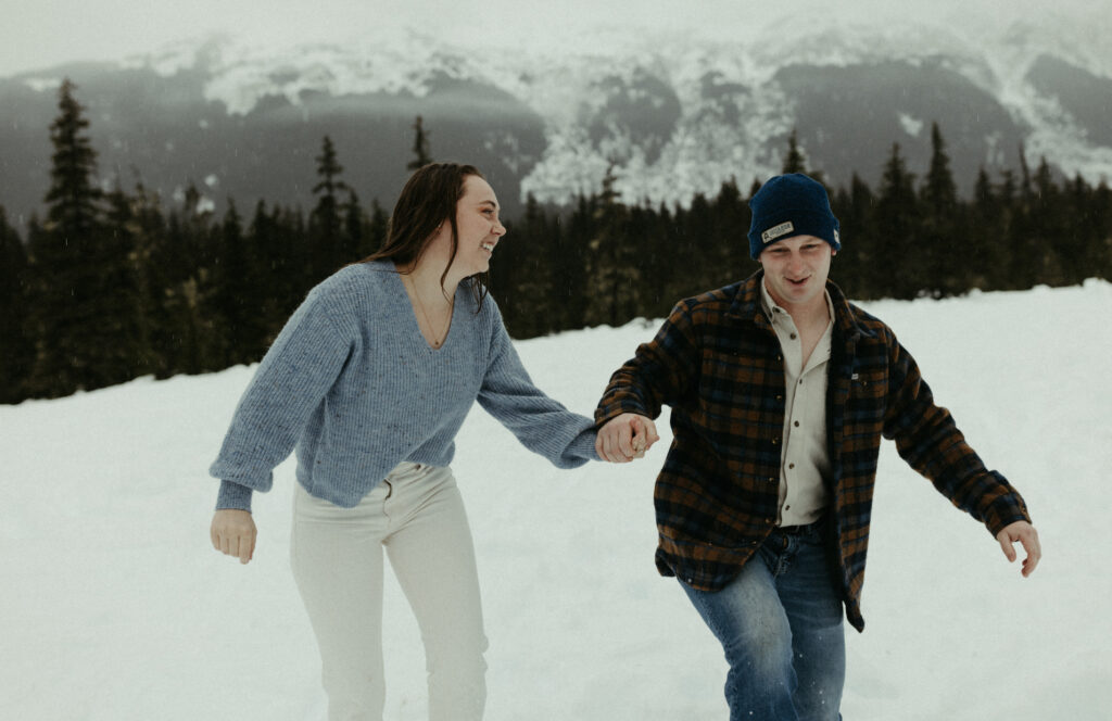 A couple holding hands and running through the snow. 