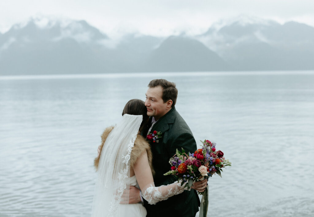 A couple embracing one another while standing next to the ocean. 