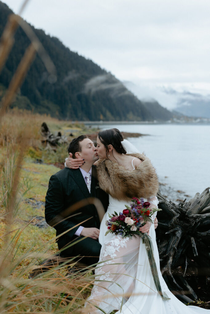 Woman holding onto man's face while sitting on a log. 