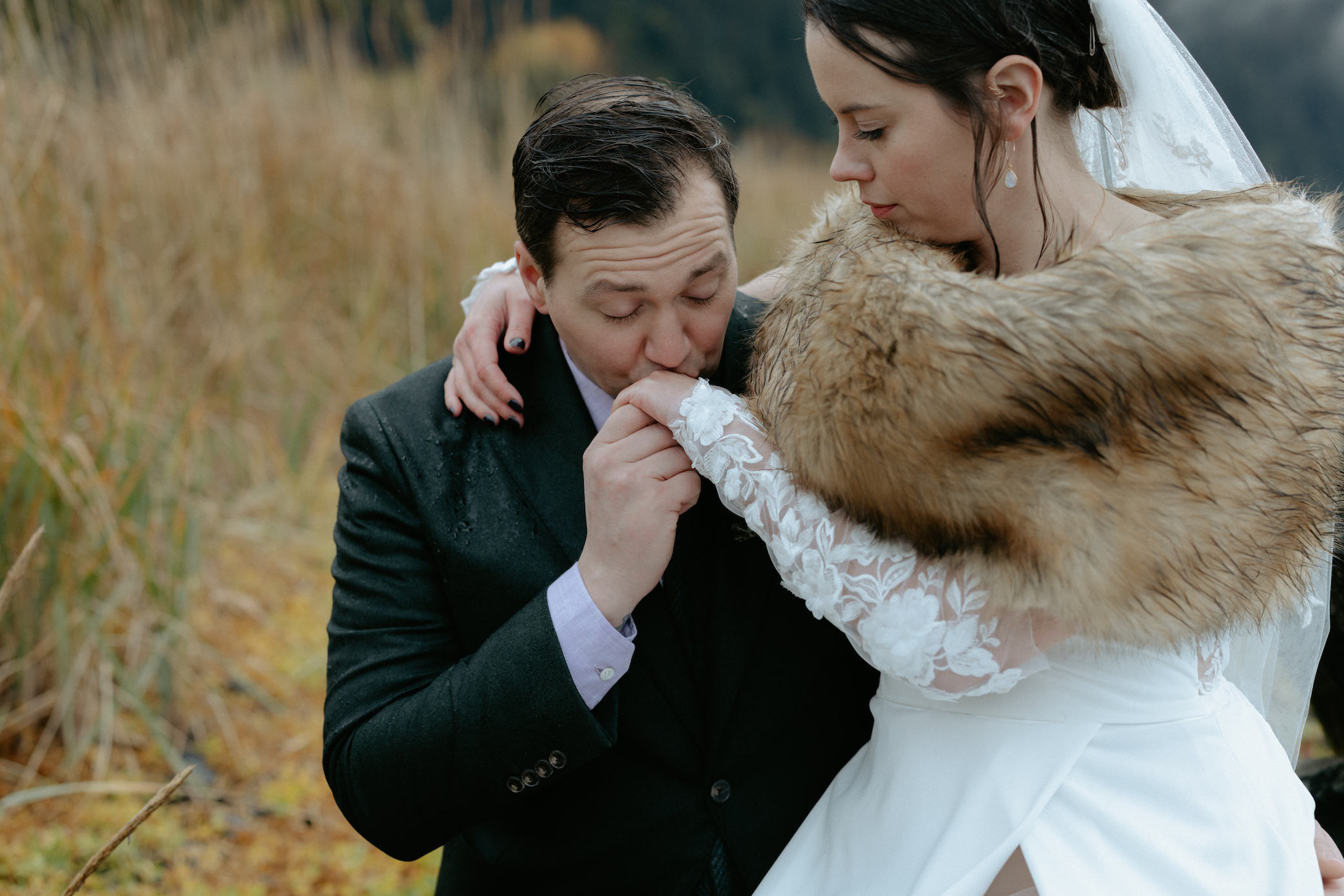 A man kissing a woman's hand while eloping in Seward, Alaska. The two are surrounded by fall foliage.