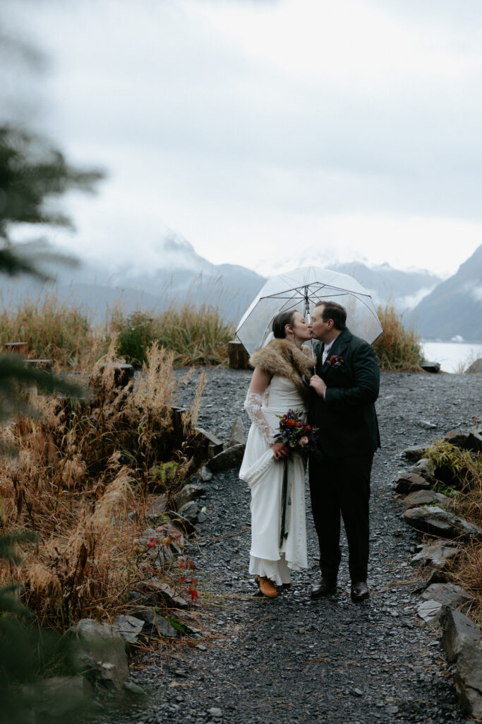 A couple walking and kissing under an umbrella. 