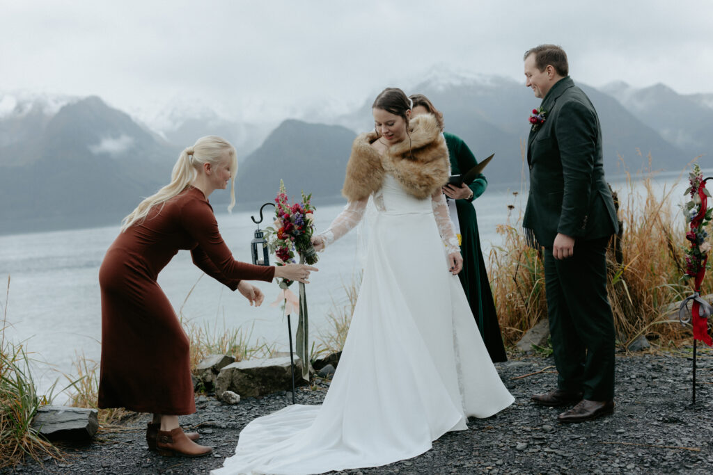 Woman passing her florals to a woman wearing a red dress and brown boots.