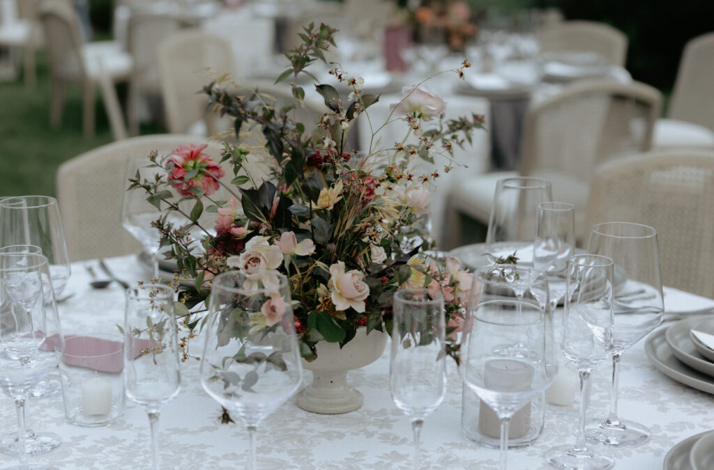 Florals and clear glasses setup on a table with white linens. 