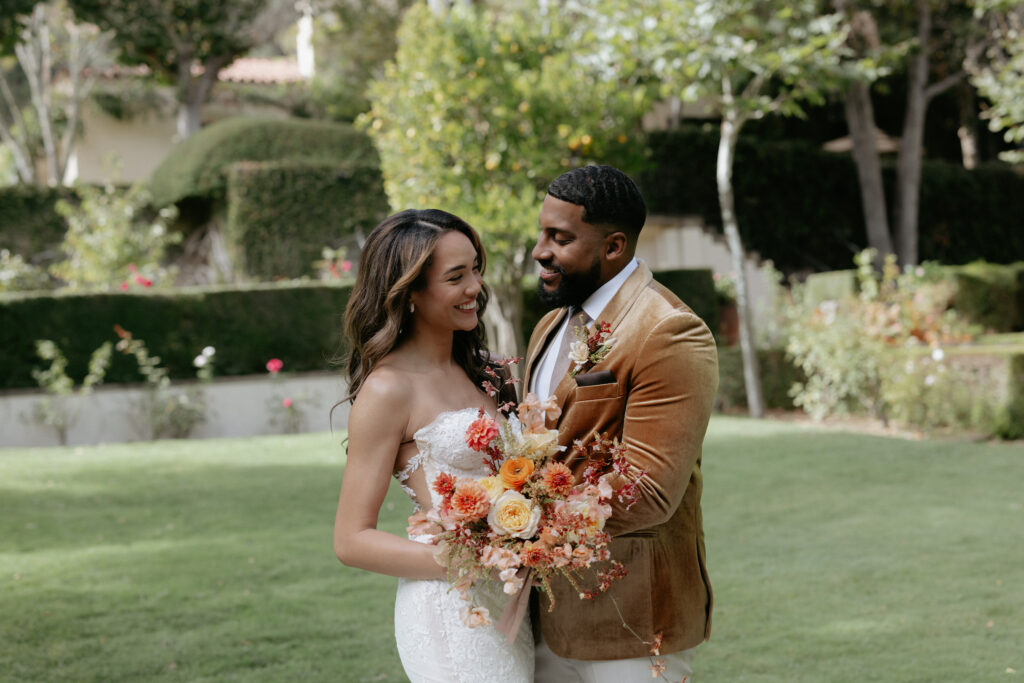 A couple standing belly button to belly button while holding onto a colorful bouquet of flowers.