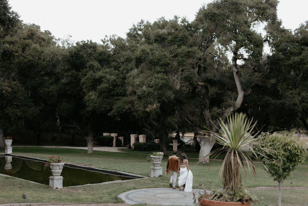 A couple walking while holding hands towards a pool of water. 