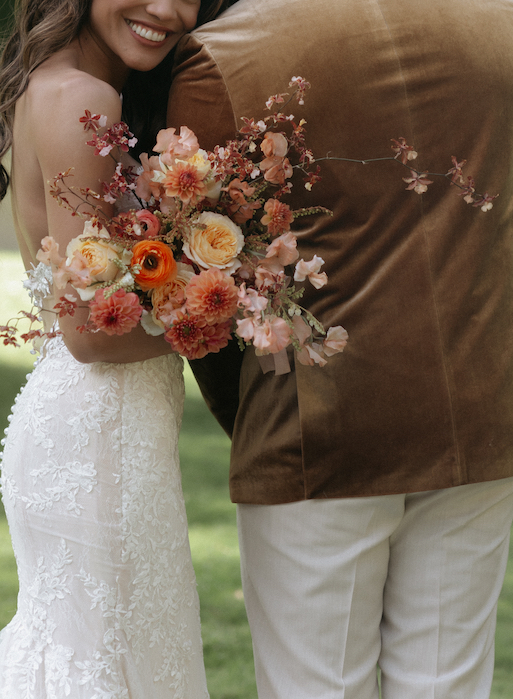 A woman holding a vibrant bouquet of florals while holding onto her partner.