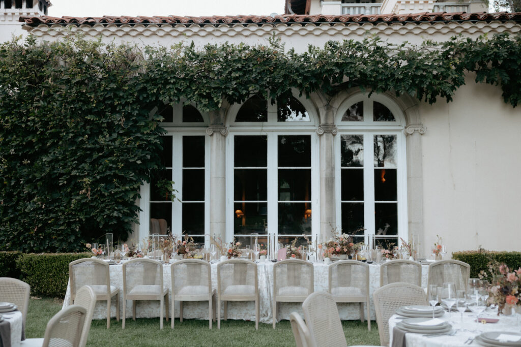 A long rectangular table with neutral colored chairs in front of a wedding venue