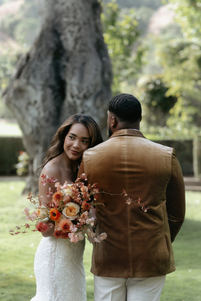 A woman snuggled into a man's shoulder while holding her bouquet near her face. 