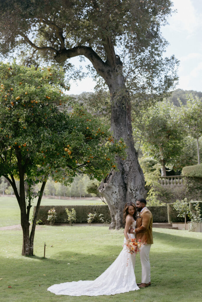 A couple standing next to a orange while snuggled up to one another. 