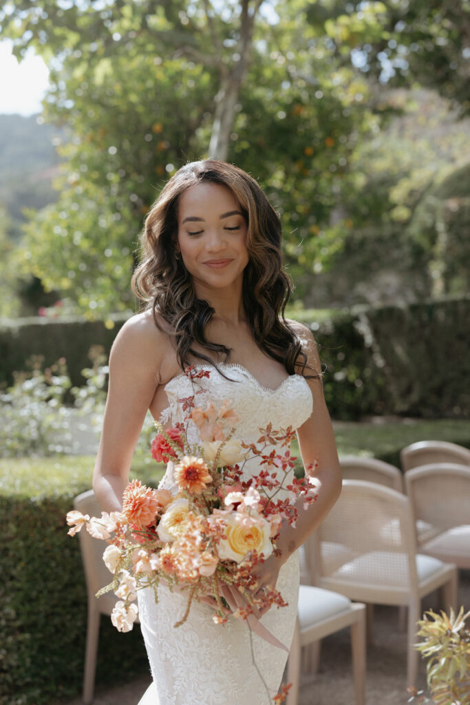 A woman wearing a white dress while holding a bouquet of white, pink and orange florals. 