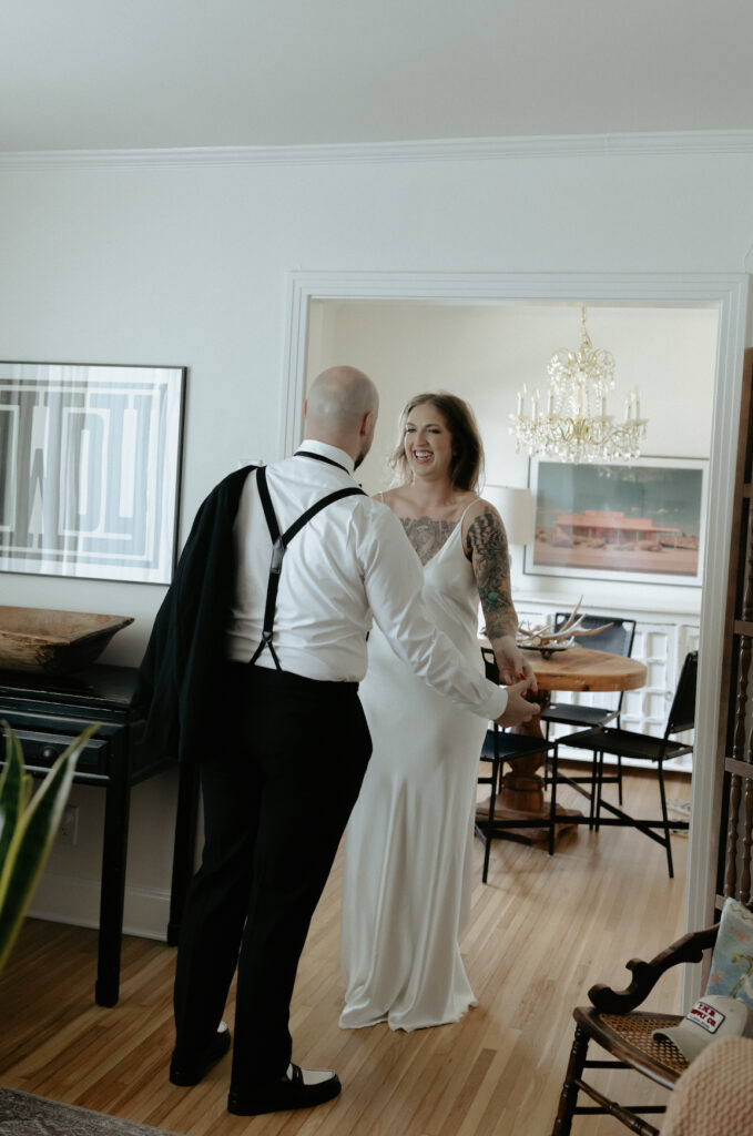 A woman smiling and holding a man's hand while wearing a white dress.