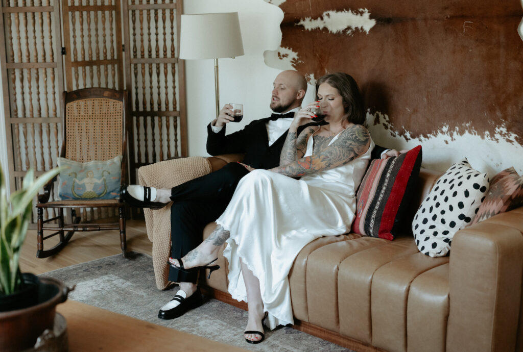 A couple sipping on a beverage while sitting on a brown couch. 