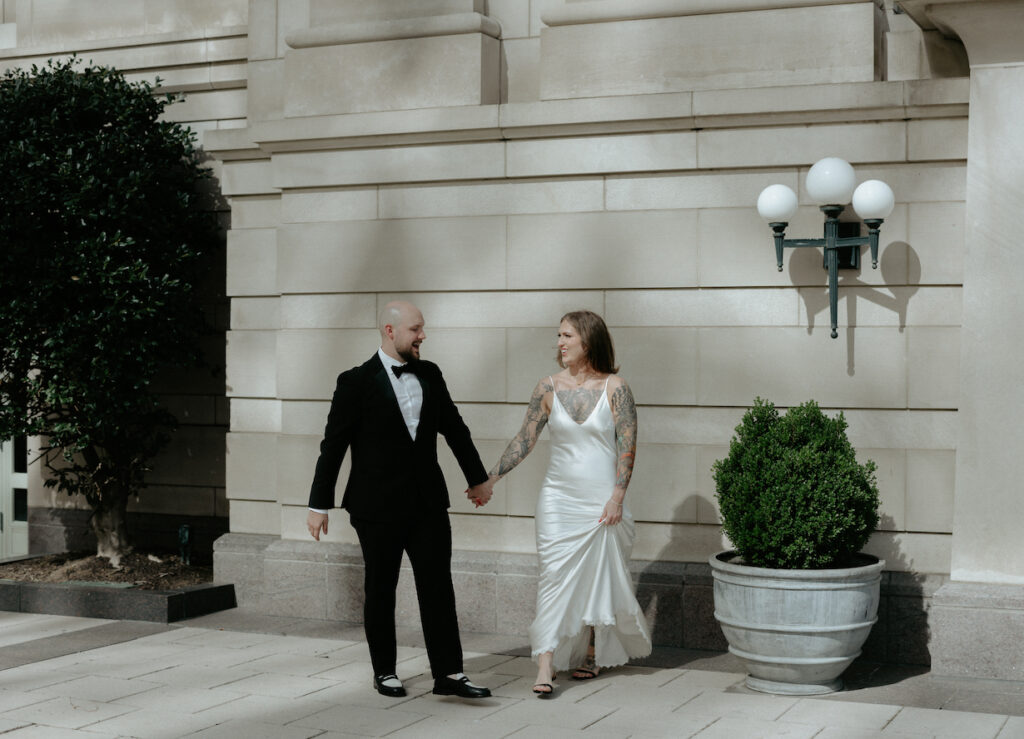 A couple walking in front of a grey building. 