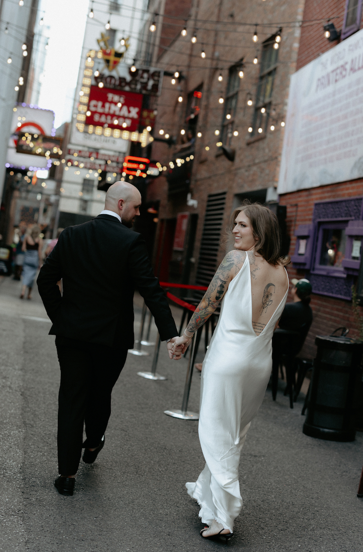 A couple holding hands and walking through a alley way. 