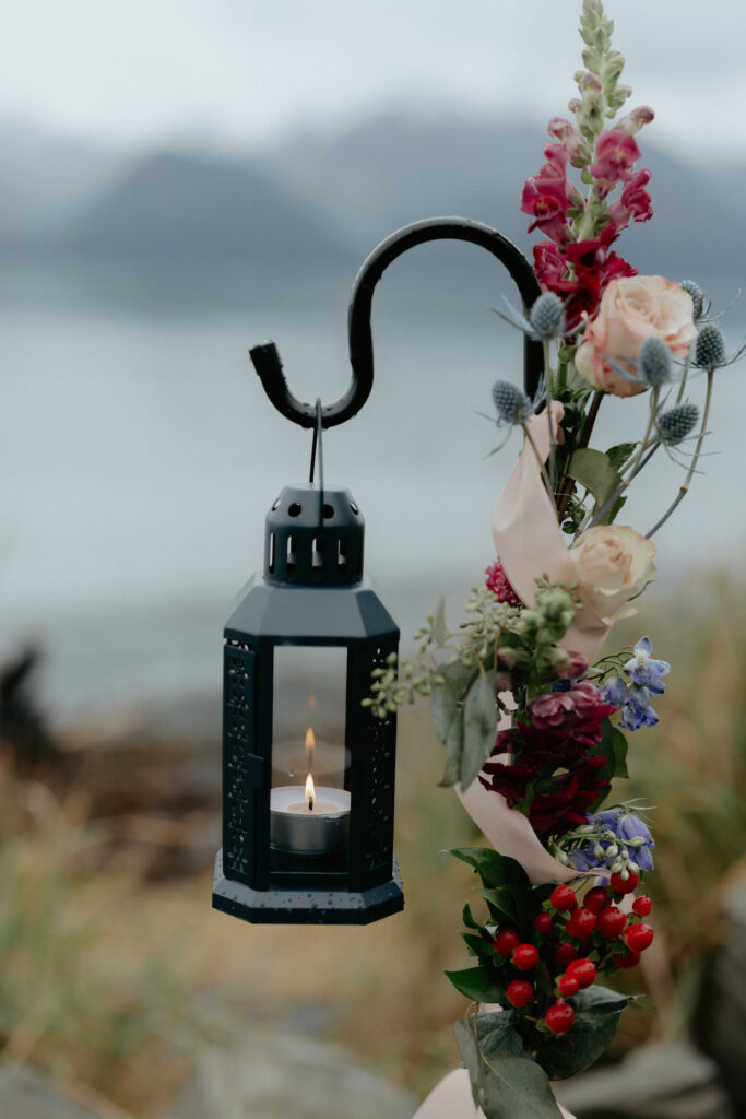 A candle inside a lantern hooked onto a arch like floral display.