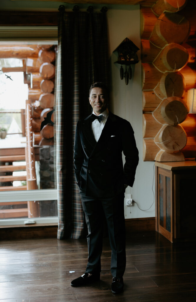 A man wearing a black suit and standing next to a window. 