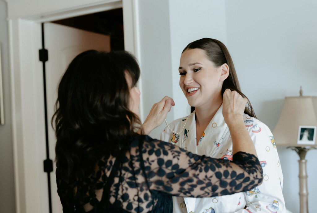 A woman putting a pearl necklace on another woman. 