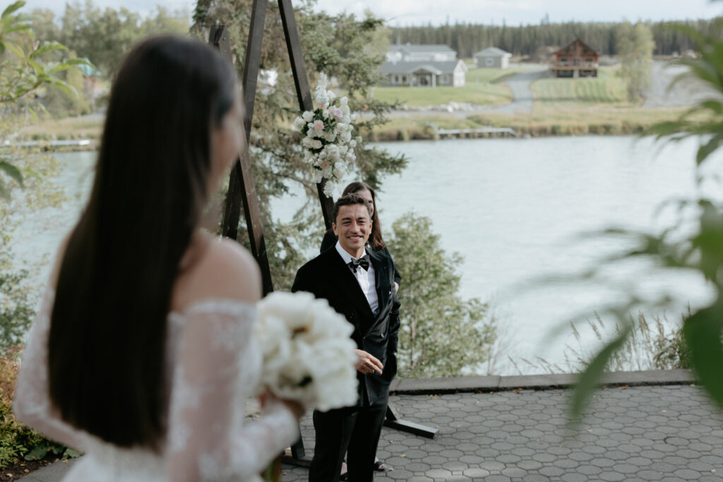 A man smiling as a woman wearing a white dress walks towards him. 