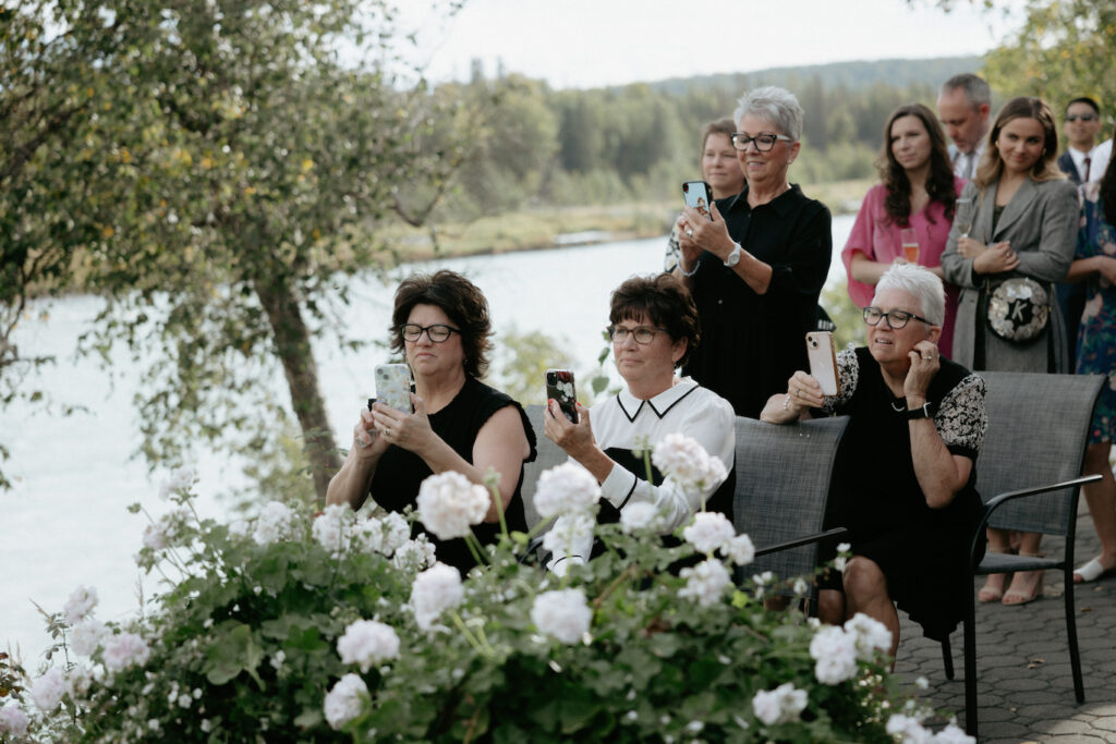 A group of woman holding phones and taking photos of the couple during the ceremony. 