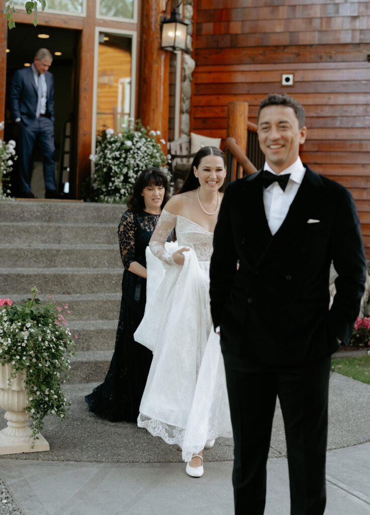 A woman walking while her mother carries her dress as they approach a man in a black suit. 