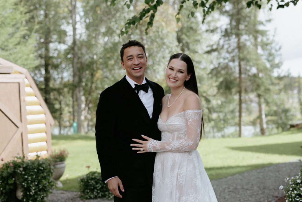 A man wearing a black suit standing next to woman wearing a white lace dress. 