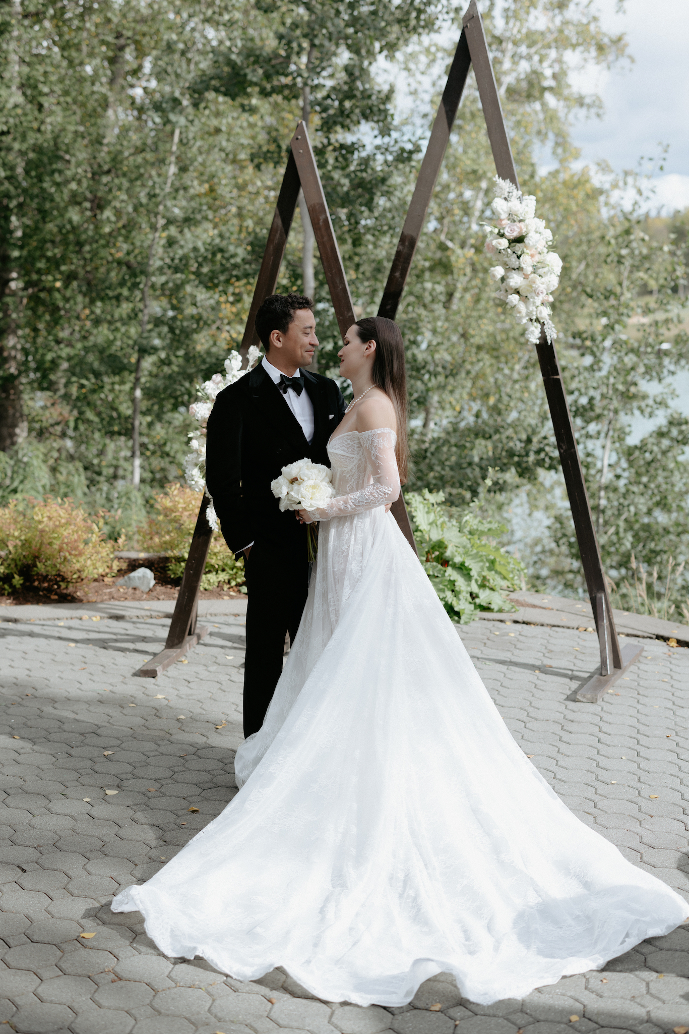 couple standing next a wooden arch in wedding attire in Alaska. 