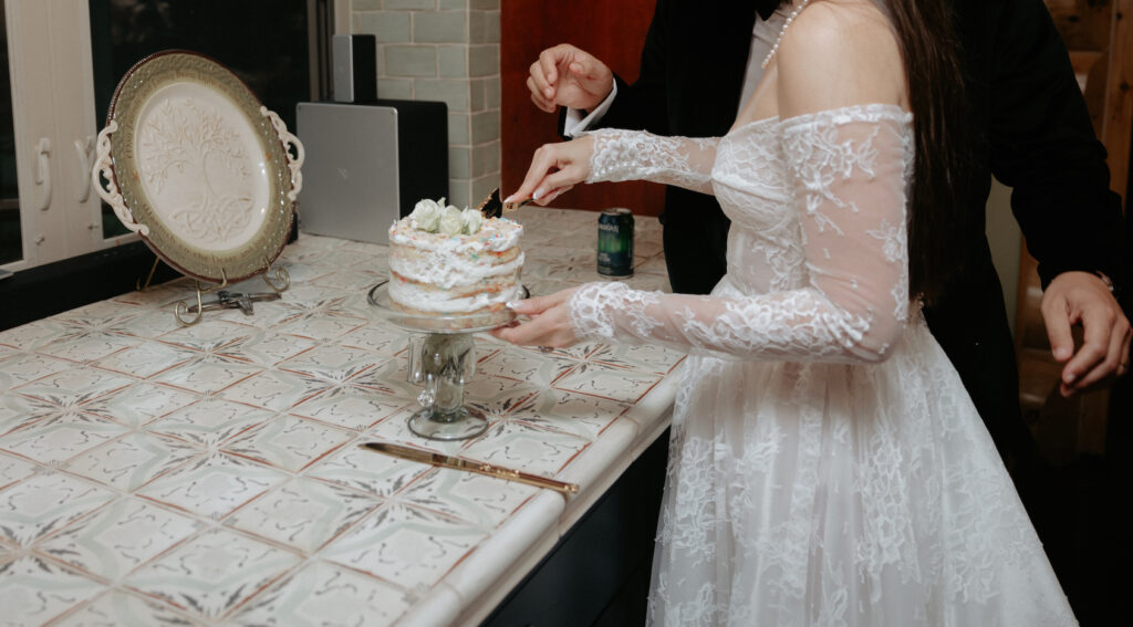 A couple cutting a small white cake. 