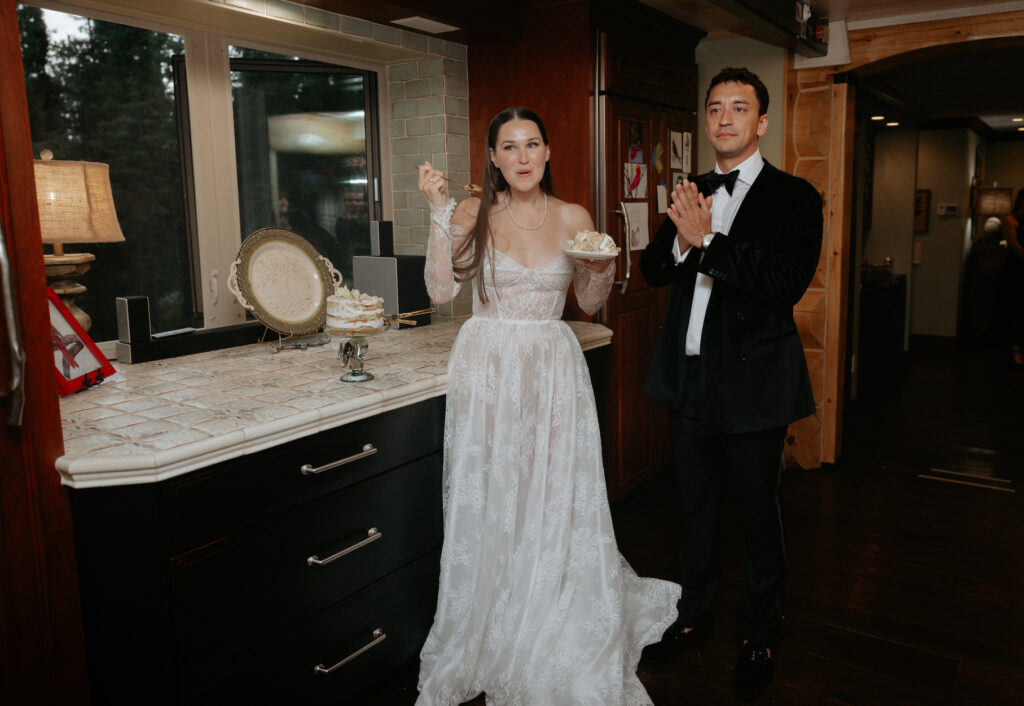 A man clapping while a woman wearing a white wedding dress eats a slice of cake.