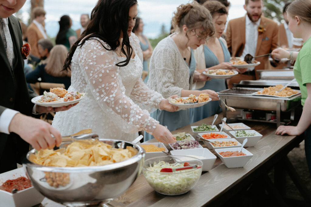 Woman putting condiments on her tacos as she goes through the buffet line at her wedding reception. 