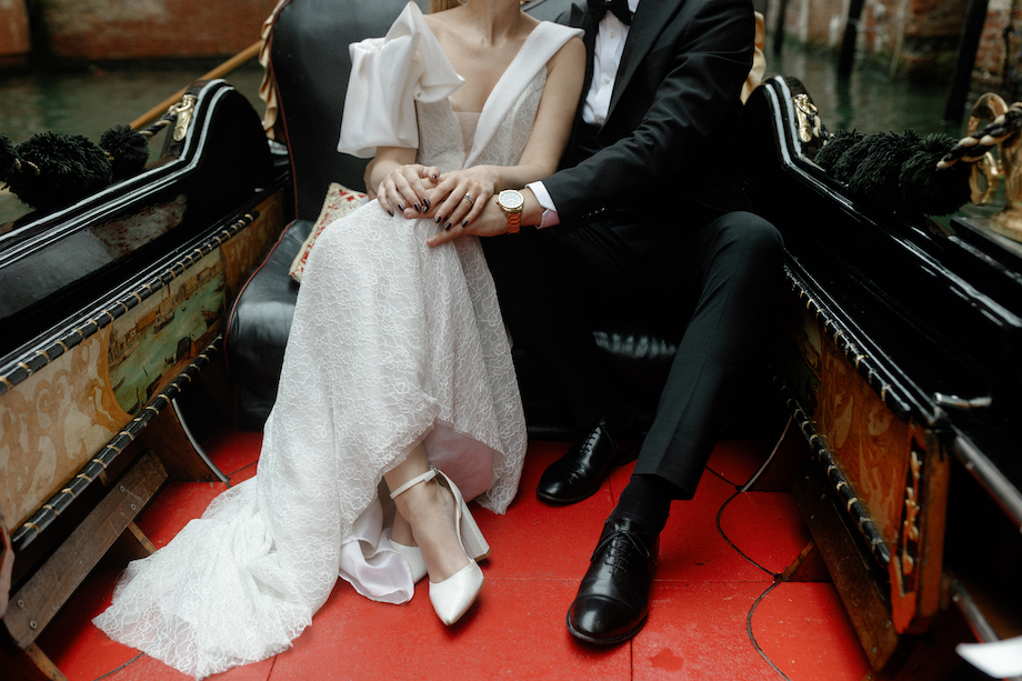 A couple holding hands while wearing wedding attire and sitting in a gondola.