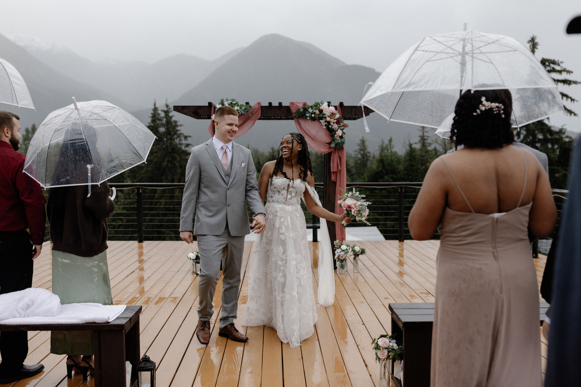 A bride and groom holding hands and walking down the aisle during their outdoor wedding in Girdwood, Alaska.