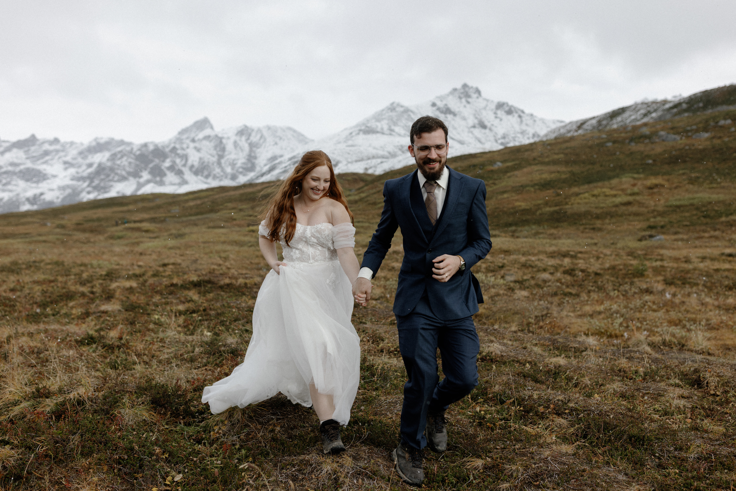 A bride and groom holding hands and running in Hatchers Pass. 